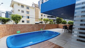 Une piscine avec un mur en briques et un revêtement de sol carrelé, entourée d’un patio aménagé avec une table et des chaises.
