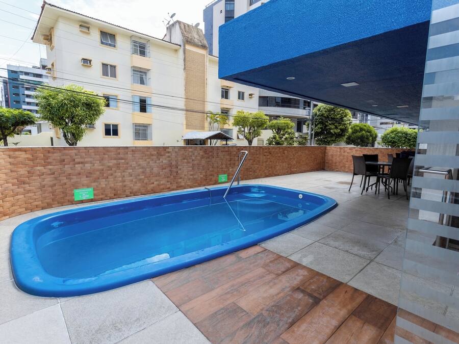 A swimming pool with a brick wall and tiled flooring, surrounded by a patio area with a table and chairs.