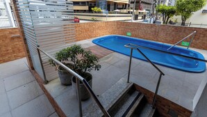 Un espace piscine aménagé sur le toit, avec une piscine bleue, des plantes en pot et un escalier menant au niveau inférieur.