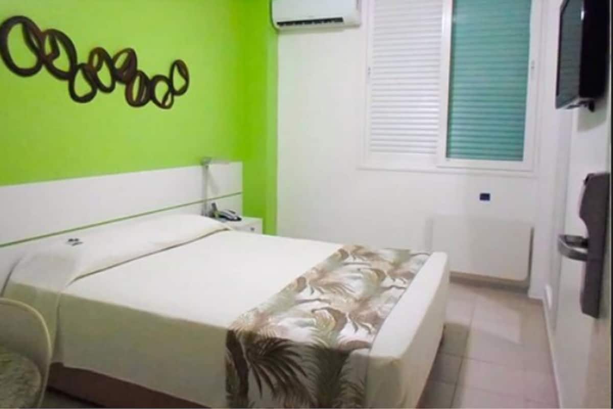 Een slaapkamer met een bed, een wandairconditioner, een raam met zonwering en een deur.