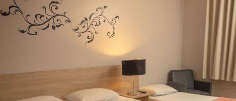 Una camera d'albergo con due letti, un comodino con lampada, una sedia e un adesivo decorativo a parete.