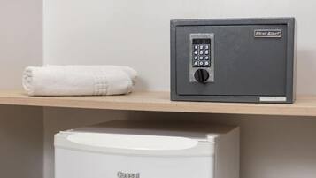 A safe with a keypad and a label reading "First Alert" on a shelf, next to a rolled-up white towel.