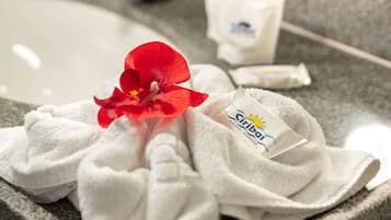 Un baño de hotel con un lavamanos, una toalla, una flor roja y un paquete de toallas con el logotipo del hotel.