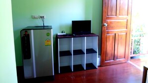A compact room with a refrigerator, a television on a small table, and a wooden door. - Rewadee Garden Resort (Koh Samui)
