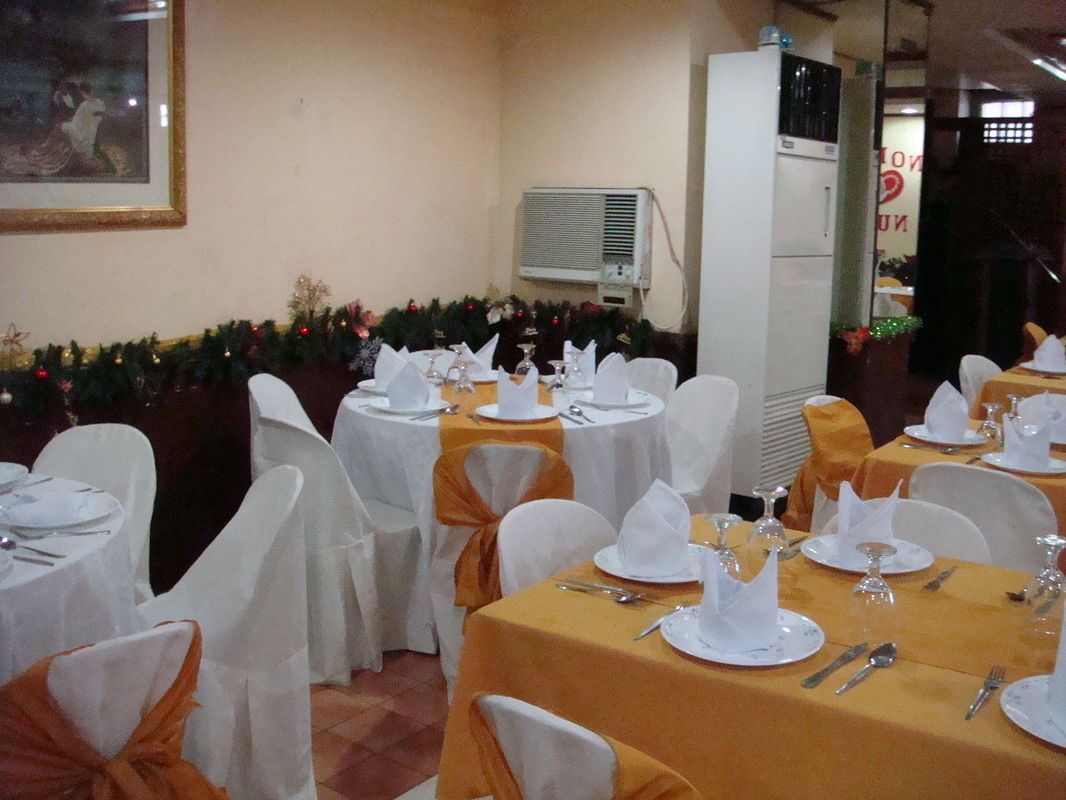 A banquet hall with round tables set for dining, white chairs with orange sashes, and a wall-mounted air conditioning unit.