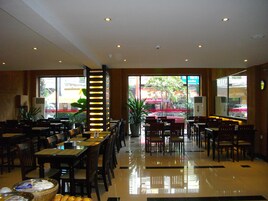 Un restaurante con varias mesas y sillas, un amplio ventanal con vista a la calle y un pilar decorativo con luces.