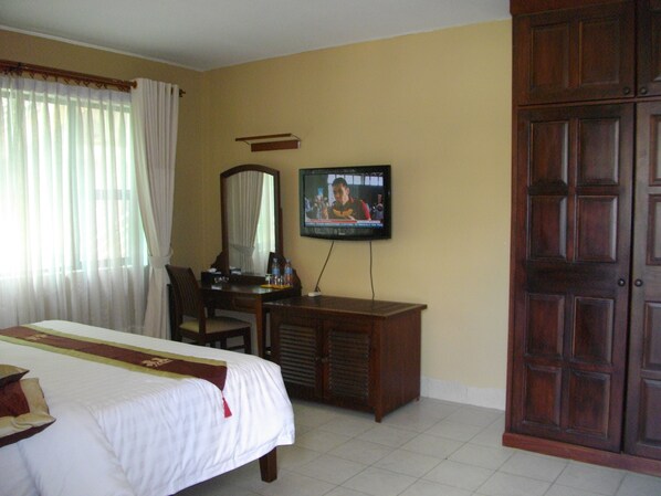 Una habitación de hotel con cama, escritorio, silla, televisor y armario.