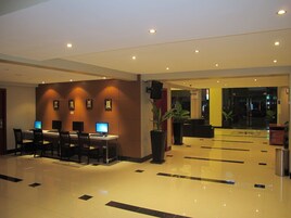 Un vestíbulo de hotel con una recepción, varias estaciones de trabajo con computadoras y una planta grande en maceta.