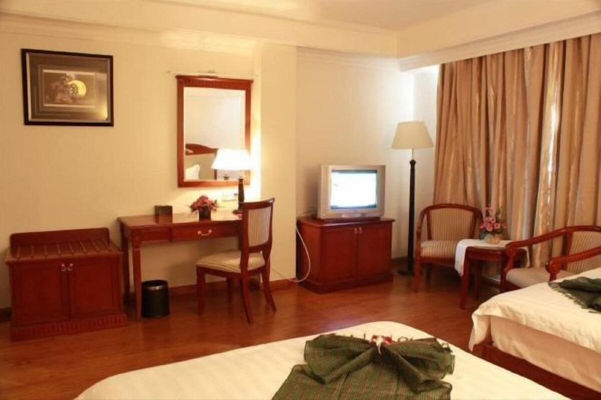 A hotel room with a bed, a desk with a computer, a chair, a television, and a lamp.