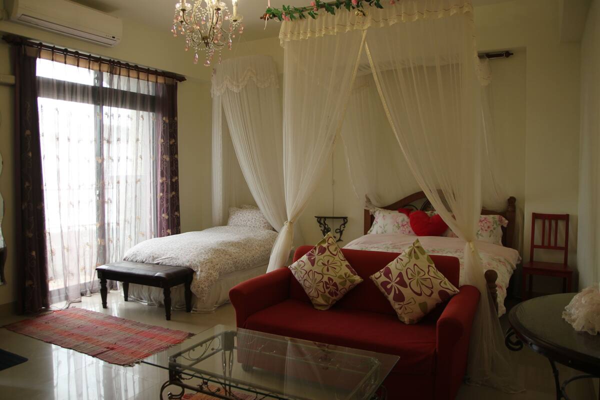 A bedroom with a bed, a red sofa, a glass coffee table, and a chair.