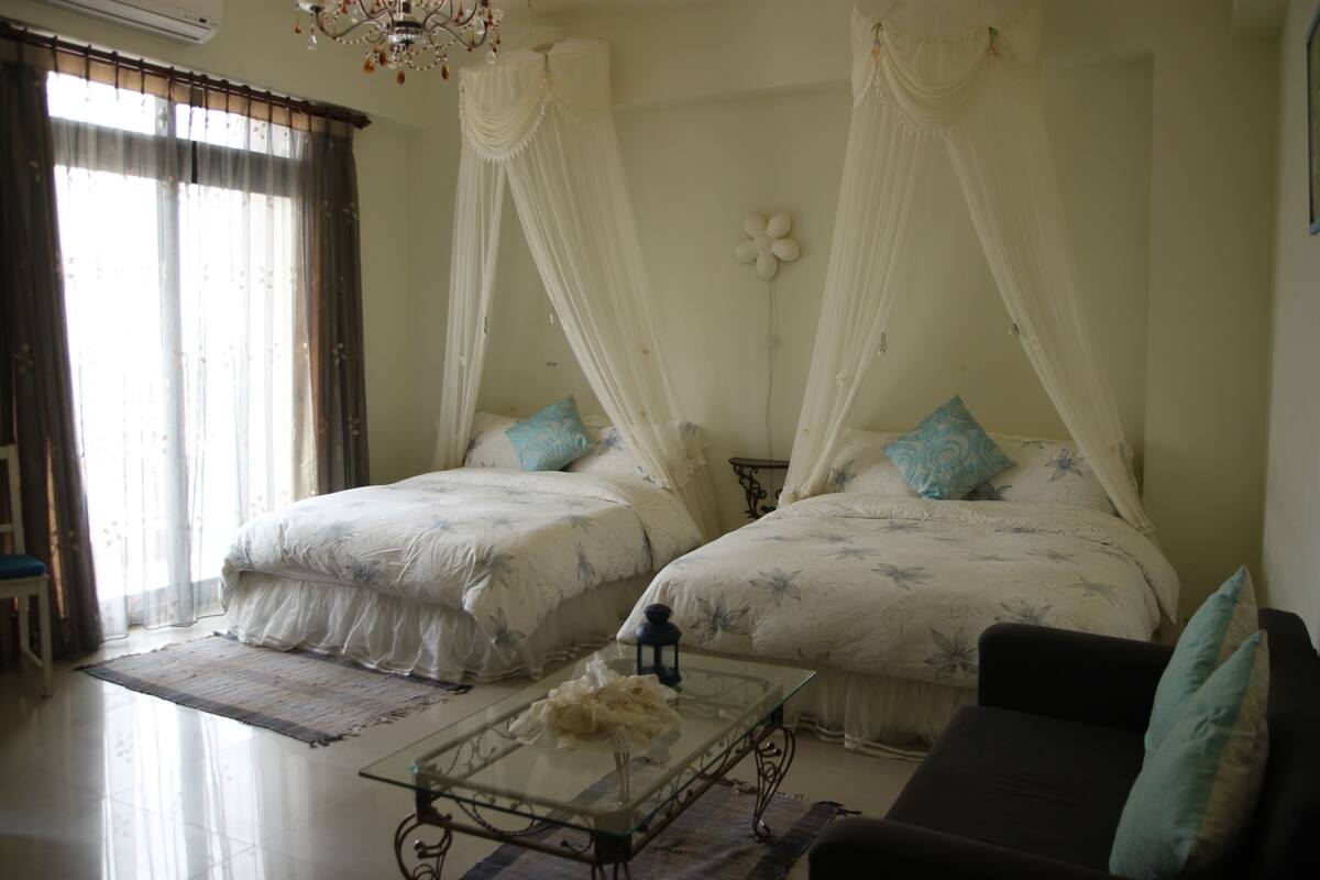 A bedroom with two beds, a glass coffee table, a sofa, and a chandelier.