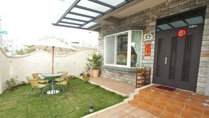 A patio with a table and chairs, a potted plant, and a door with a decorative plaque. - Blue Cotton Candy (Taitung)