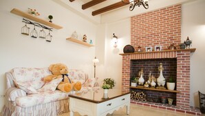 A cozy living room with a floral sofa, a large teddy bear, a glass coffee table, a brick fireplace, and decorative shelves. - Blue Cotton Candy (Taitung)