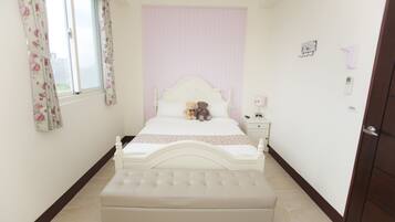 A bedroom with a white bed, a bedside table, a nightstand, and a window with floral curtains.