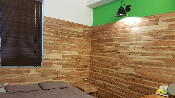 A bedroom with a wooden wall panel design, a bed, a bedside table, and a green accent wall. - Romeo B&B (Taitung)