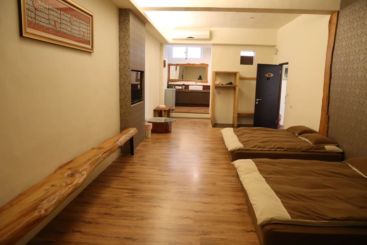 A narrow hallway with wooden flooring leading to a bedroom with two beds. A small table and a bench are visible in the hallway.