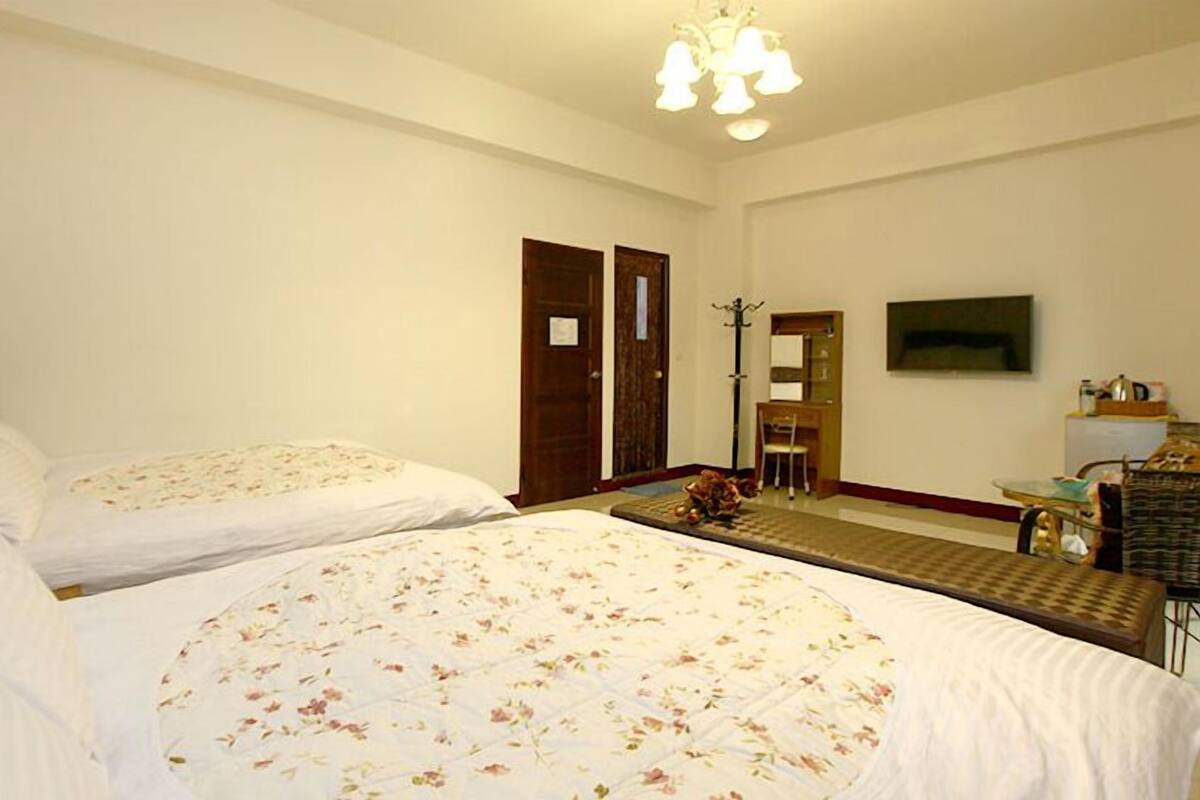 Quarto de hotel com duas camas, uma escrivaninha, uma cadeira, uma televisão e uma porta.