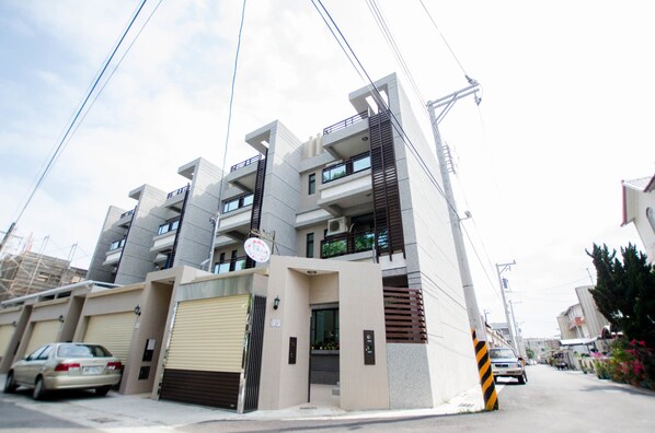 A modern multi-story residential building with balconies, a garage, and a street view.