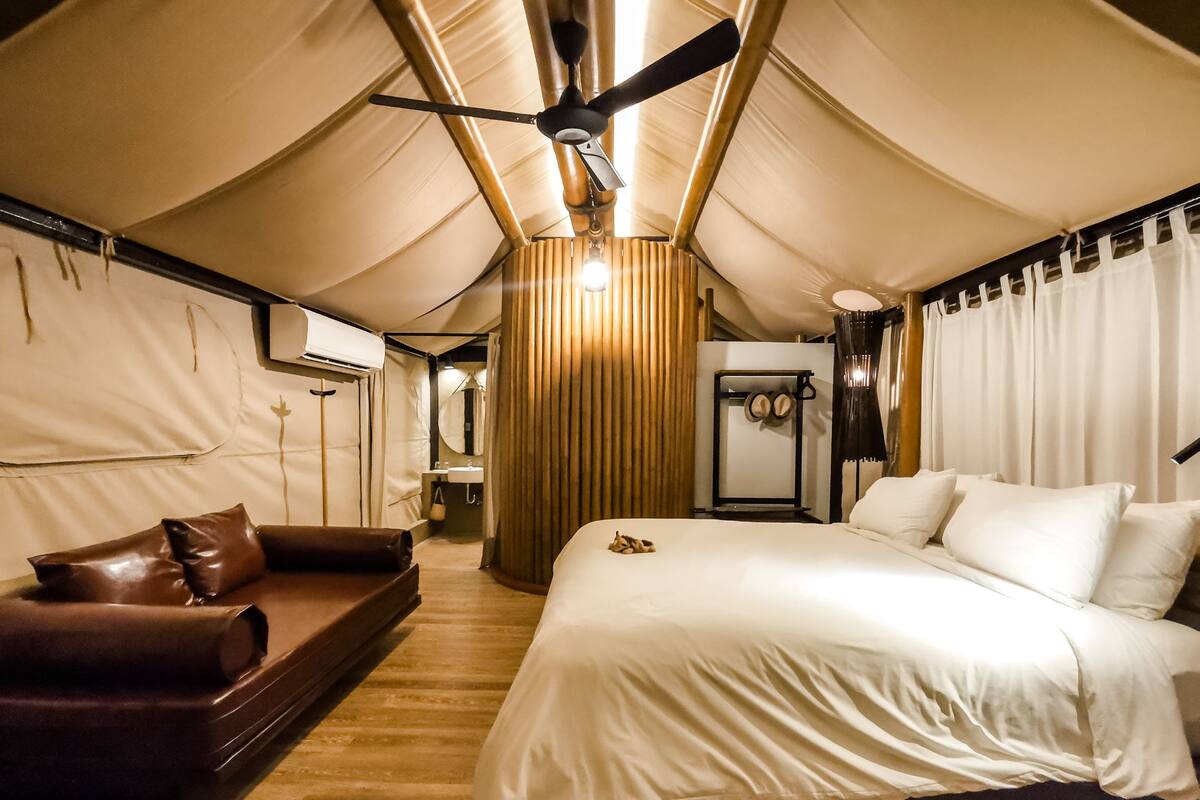Een ingerichte tent met een bed, een bank en een plafondventilator.