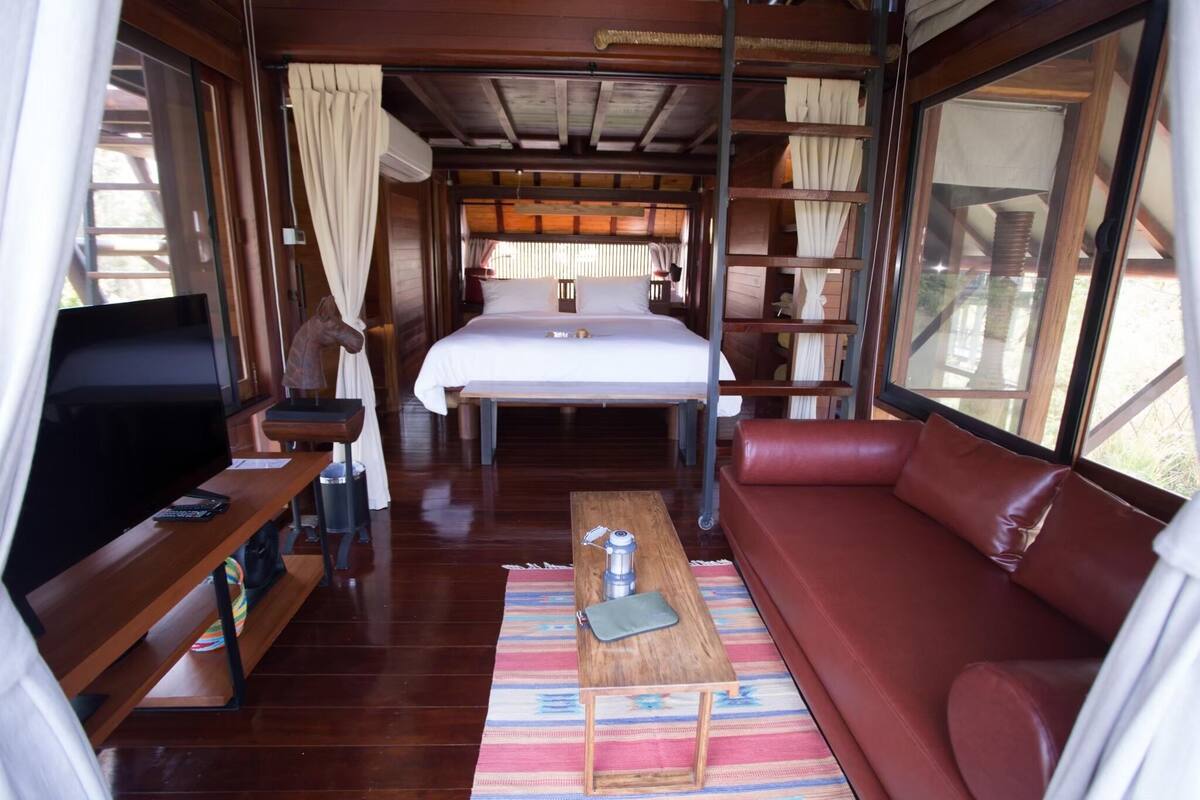 Een kleine kamer met een bed, een televisie, een koffietafeltje en een rode bank.