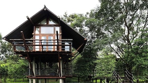 A wooden cabin with a balcony, surrounded by lush greenery and a small wooden bridge. - Lala Mukha Tented Resort Khao Yai (Pak Chong)
