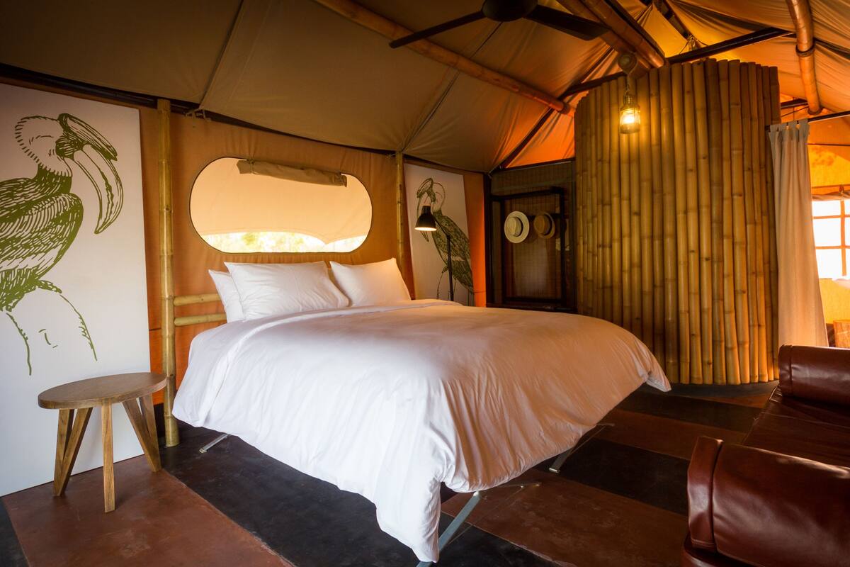 Een kamer met een bed, een stoel, een muur met een vogelmuurschildering, een lamp en een bamboemuur.