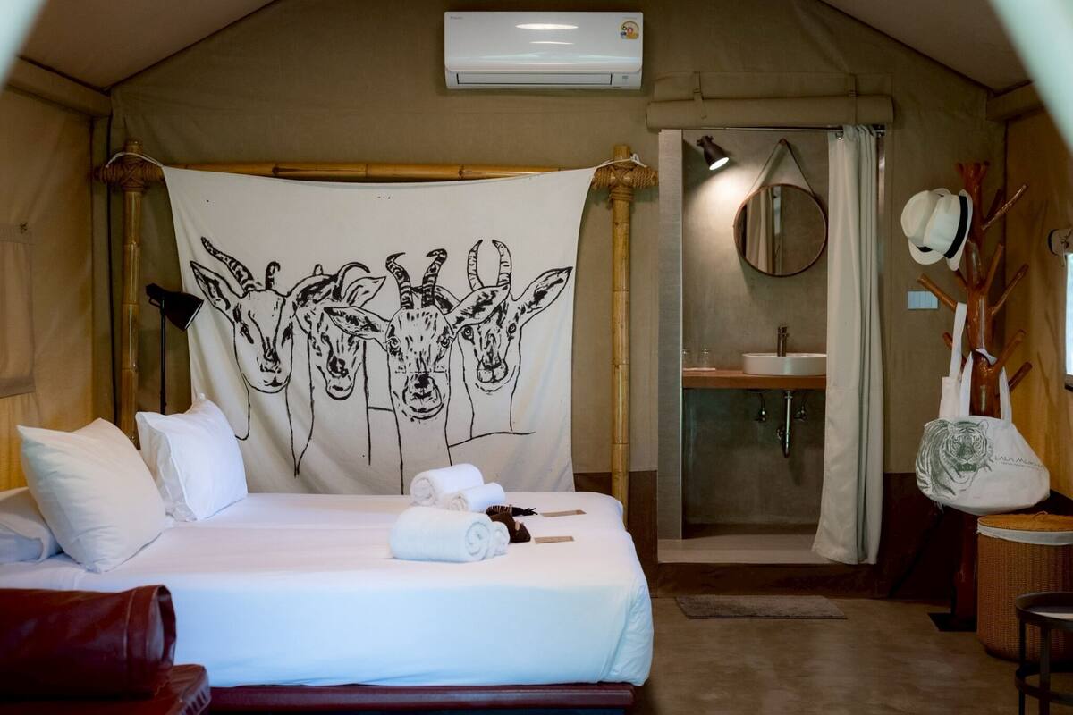 Een tentvormige kamer met een bed, douche, wastafel en een ophangrek voor handdoeken.