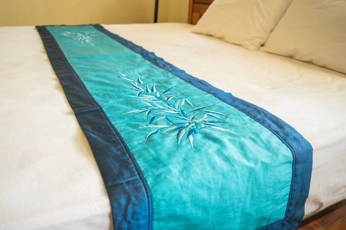 A bed with a white mattress and a teal bedspread with a leaf pattern.