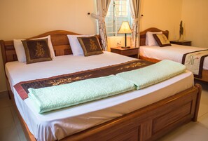 Una cama doble con cabecera de madera, dos mesitas de noche con lámparas y una ventana con cortinas.