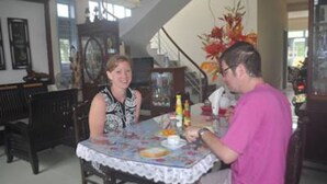 A dining area with a table set for two, surrounded by dark wooden furniture. - Areca Homestay (Da Nang)