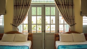 A room with two beds, a large window with curtains, and a view of greenery outside. - Areca Homestay (Da Nang)