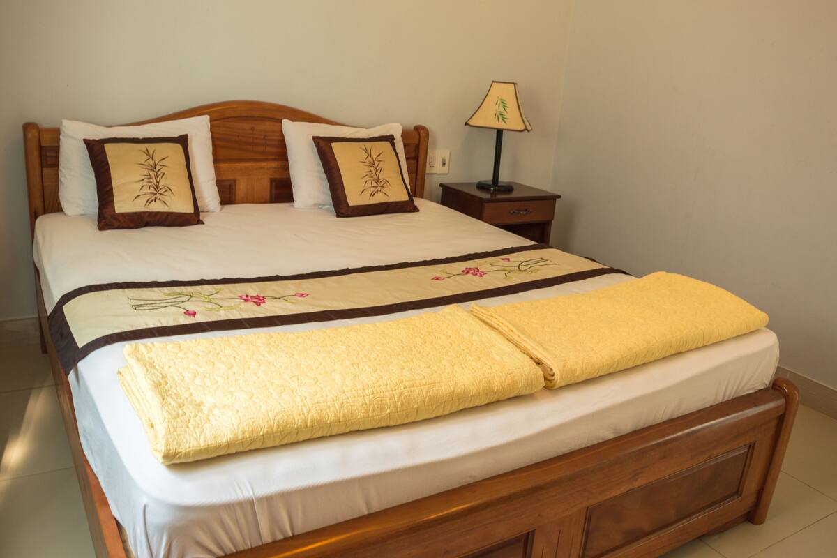 A neatly made bed with a floral bedspread, two pillows with a bamboo design, and a bedside table with a lamp.