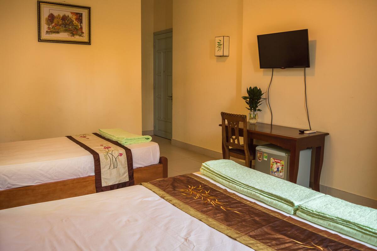 A hotel room with two single beds, a desk with a television, and a small refrigerator.