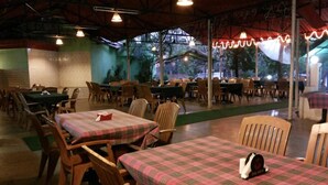 A restaurant with tables covered in plaid tablecloths and wooden chairs. - The Sincro Hotel (Margao)