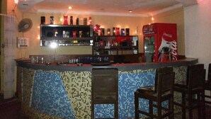 A bar area with a tiled counter, shelves with bottles, a fan, and a Coca-Cola refrigerator. - The Sincro Hotel (Margao)