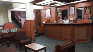 A reception area with a counter, chairs, and a staircase. - The Sincro Hotel (Margao)