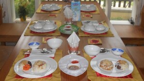 A dining table set with plates, bowls, and cutlery, with a carton of milk and a glass pitcher on the table. - Lila Homestay Hoi An (Da Nang)