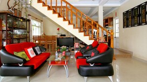 A spacious living room with a red and black sofa set, a wooden staircase, and a television in the background. - Lila Homestay Hoi An (Da Nang)