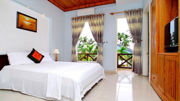 A hotel room with a bed, a TV, and a balcony with curtains. - Lila Homestay Hoi An (Da Nang)