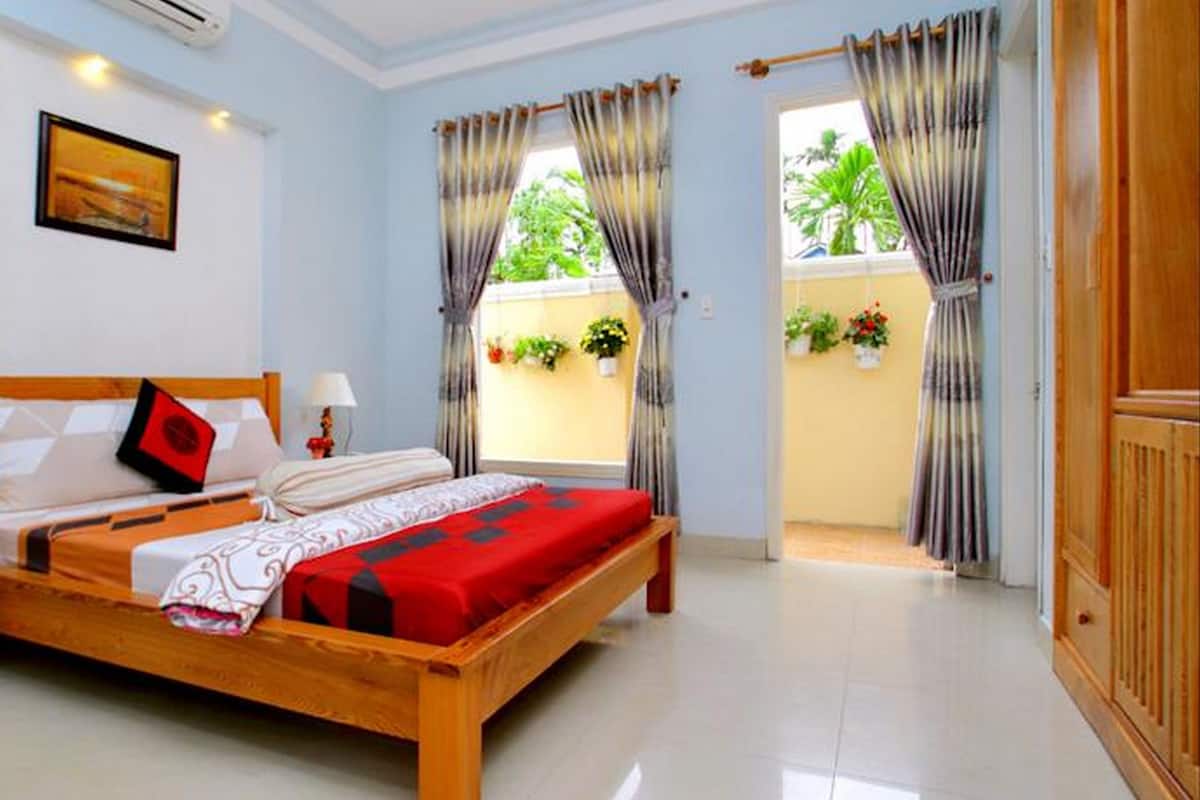 A hotel room with a wooden bed, two bedside tables, a nightstand, a window with curtains, and a view of greenery outside.
