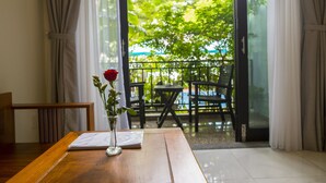 An indoor dining area with a wooden table, a vase with a single red rose, and a view of an outdoor patio with chairs and a table. - Magnolia Garden Villa (Da Nang)