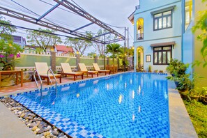 A swimming pool with lounge chairs and a covered area, surrounded by greenery and a building with balconies. - Magnolia Garden Villa (Da Nang)