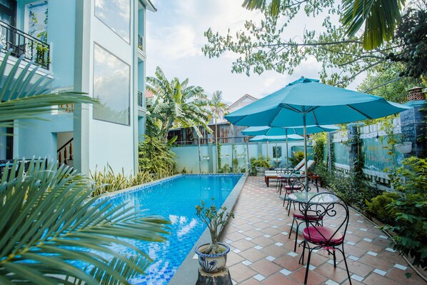 A pool area with a tiled deck, outdoor seating, and a large umbrella. - Magnolia Garden Villa (Da Nang)