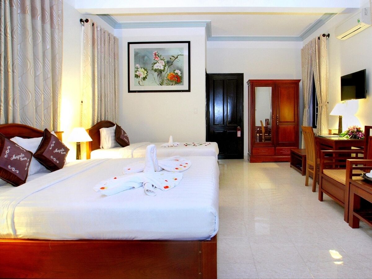 A hotel room with two beds, a dining area, and a mirror.