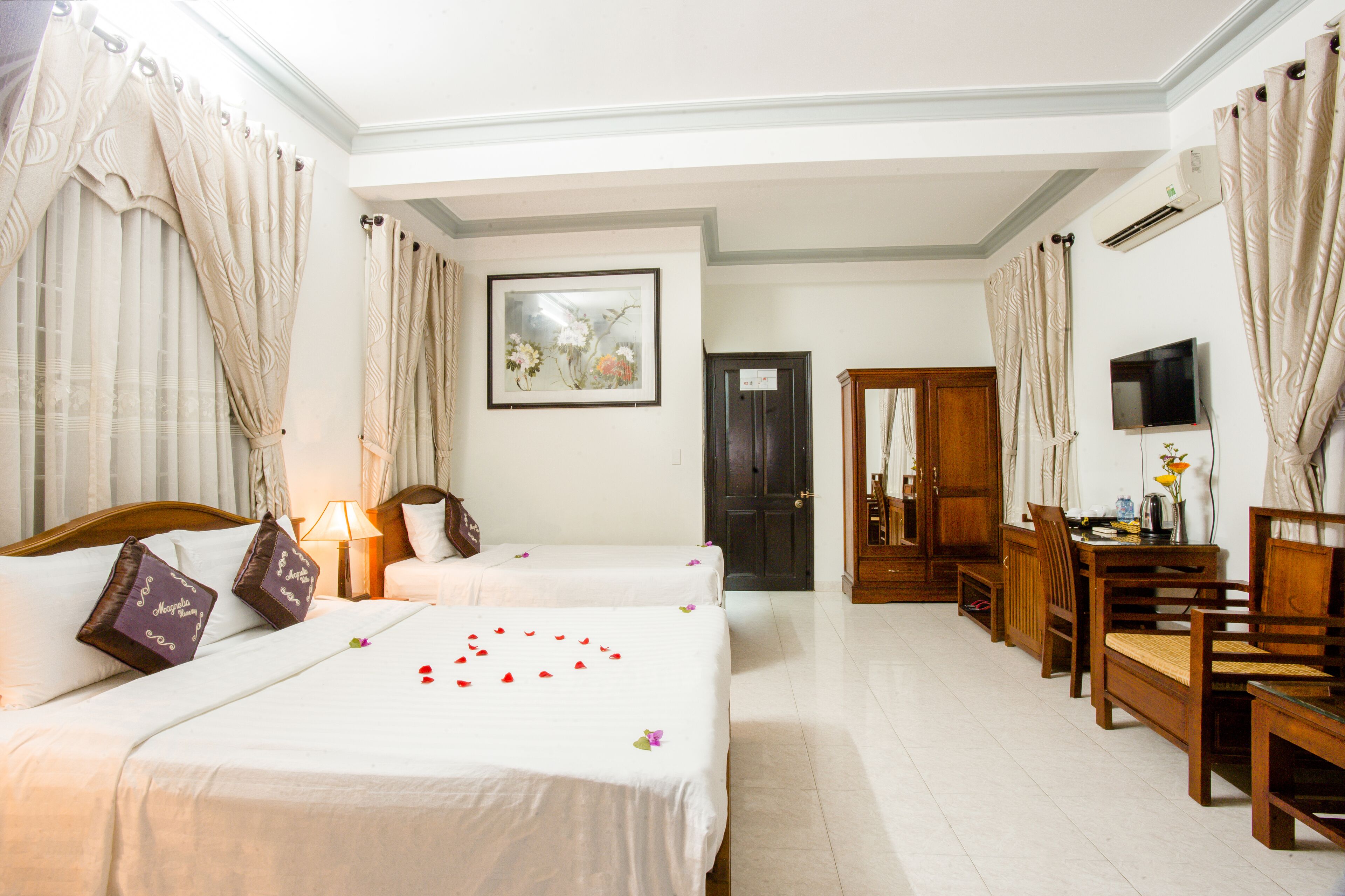 A hotel room with two beds, a desk with chairs, a television, and a door leading to another room.