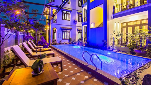 A pool area with lounge chairs and a dining table, surrounded by potted plants and a staircase leading to upper floors. - Magnolia Garden Villa (Da Nang)