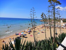 Una playa con gente nadando y tomando el sol, sombrillas y sillas de playa.