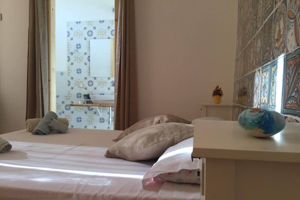 A bedroom with a bed, pillows, a bedside table, and a window with curtains.