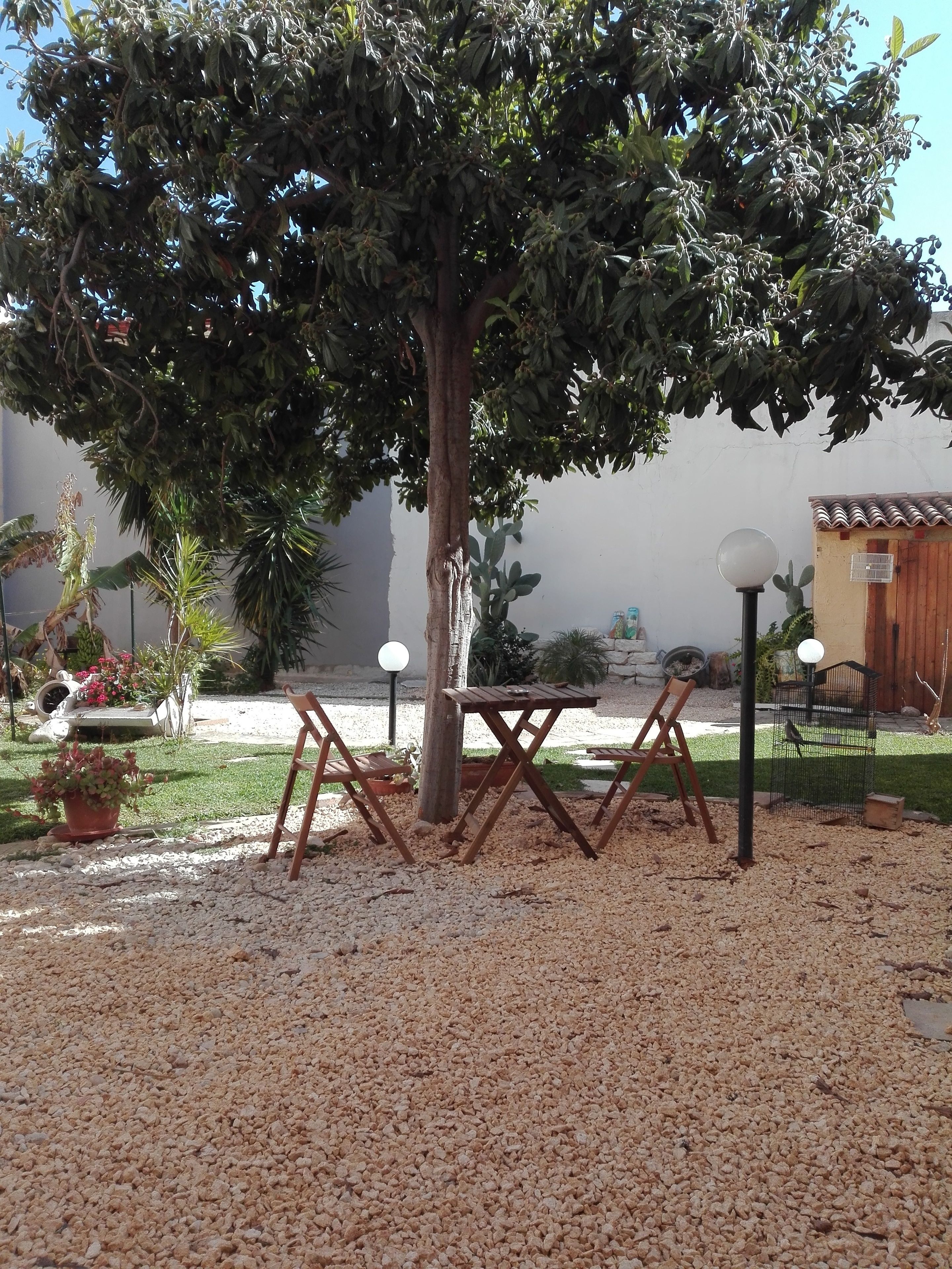 A patio area with a table and chairs, surrounded by gravel, under a tree.
