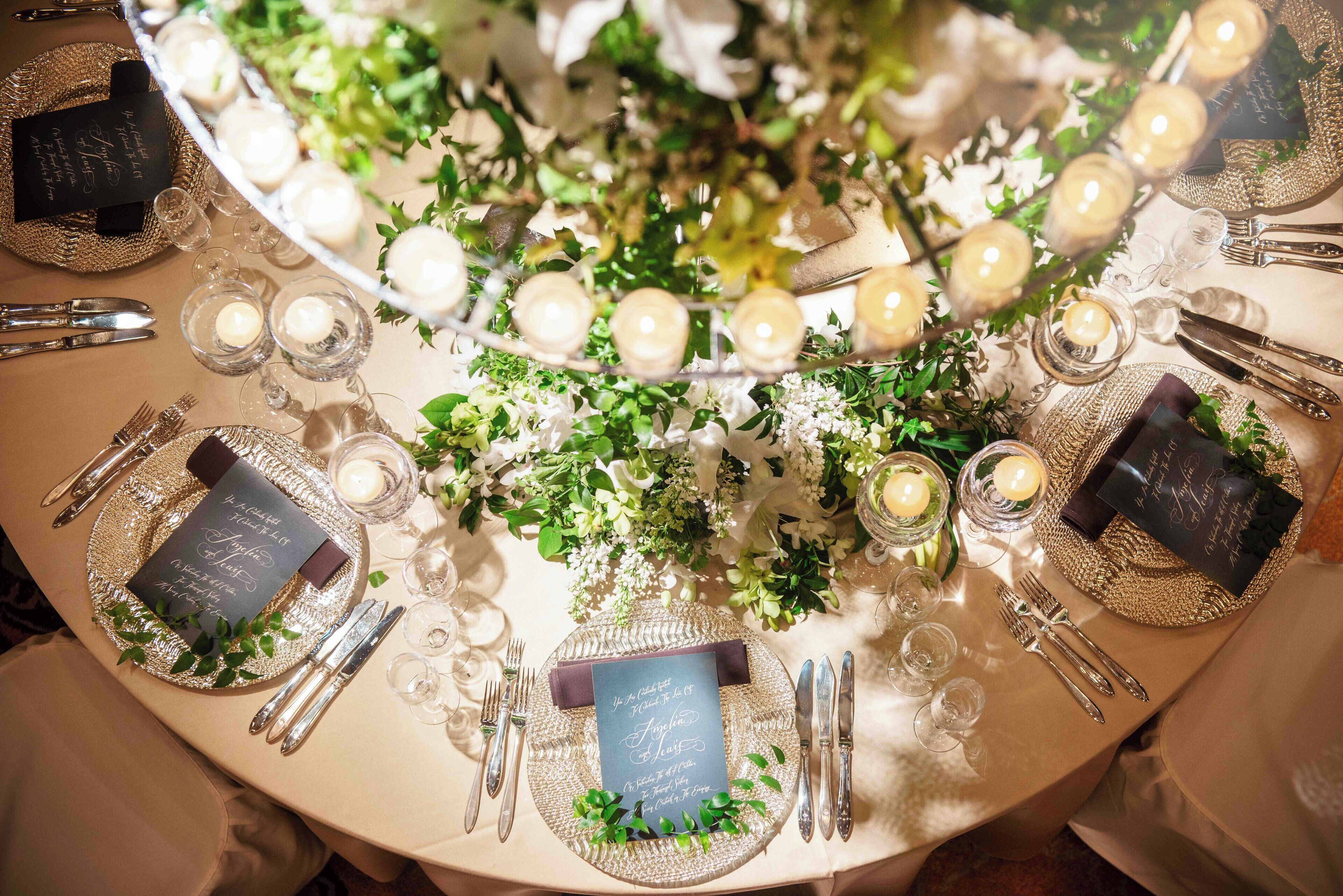 Una mesa redonda dispuesta para un evento formal, con cristalería, velas y adornos florales.